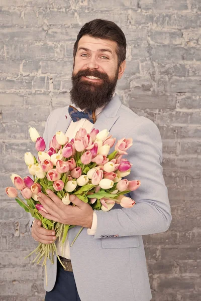 Romantic gift. Macho getting ready romantic date. Tulips for sweetheart. Man well groomed wear blue tuxedo bow tie hold flowers bouquet. Waiting for his girlfriend. Romantic man with flowers