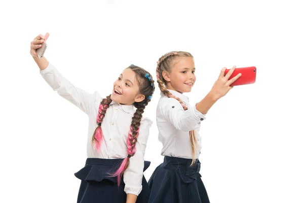 Verdadeiras estrelas selfie. Pequenas alunas felizes tomando selfie com smartphones isolados em branco. Crianças sorrindo para selfie câmeras em telefones celulares. Sessão de selfie em 1 de setembro — Fotografia de Stock