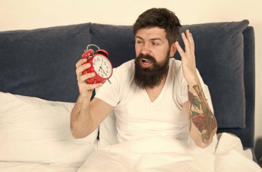 Çalar saat ile kaldırın. Yine uyuya kalmışım. Erken uyanma için ipuçları. Erken bir yükseltici olmak için ipuçları. Adam hipster uykulu yüz ile çalar saat yatakta sakallı. Sabah erken uyanma ile sorun