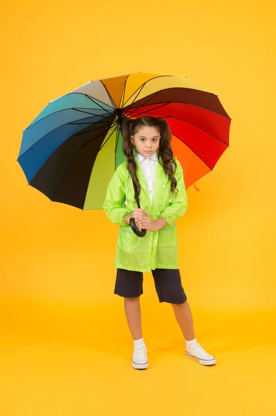 Andare a scuola giorni di pioggia più divertente con accessori luminosi. La pioggia non è così male se hai vestiti resistenti all'acqua. Studentessa spensierata colorato ombrello indossare impermeabile impermeabile impermeabile. Pioggia autunnale — Foto Stock