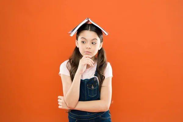 Huiswerk concept. Homeschooling en privéles. Boek op haar hoofd. Kleine meisje boek dak hoofd. Kleine meisje boek oranje achtergrond. Interessant verhaal voor Kid. Studeren en ontspannen. Studeren thuis — Stockfoto