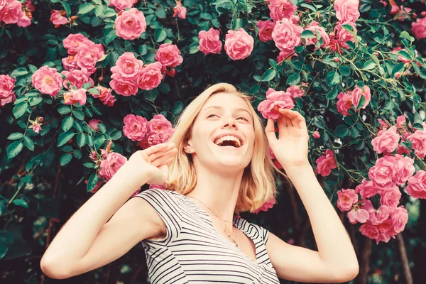 Parfüm ve kozmetik. Çiçek açan gül çalı önünde kadın. Yaban gülleri çiçeği. Gizli Bahçe konsepti. Güller kokusu. Pembe Bloom kız Sevimli sarışın koklama koku. İlkbahar ve yaz