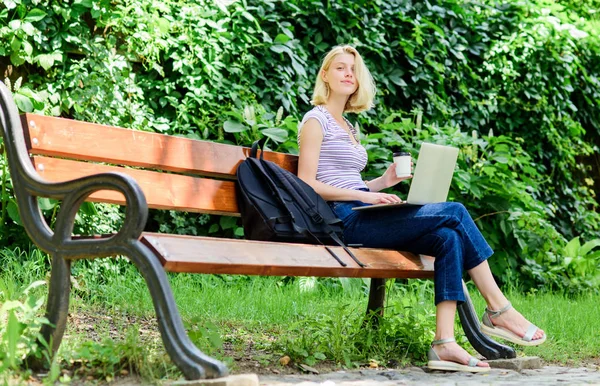 Navegar por Internet. Vida estudiantil moderna. Estudiante normal. Chica estudiante adorable con portátil y taza de café sentarse banco en el parque. Estudia al aire libre. Una estudiante trabaja con un cuaderno. Aprender a estudiar explorar — Foto de Stock