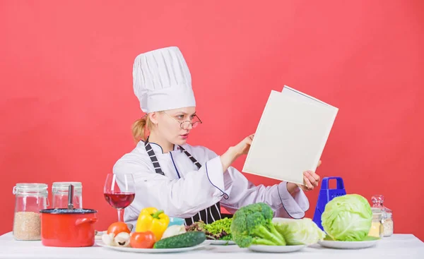 Woman chef cooking healthy food. Girl read book top best culinary recipes. Culinary school concept. Female in hat and apron knows everything about culinary arts. Traditional cuisine. Culinary expert