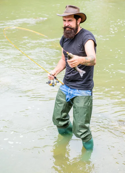 Uomo brutale indossare stivali di gomma stare in acqua del fiume. Attività del fine settimana Fisher. Pescatore con attrezzatura da pesca. Pesce all'amo. Tempo libero nella natura selvaggia. Divertimento della pesca è la cattura. Pesca hobby maschile — Foto Stock