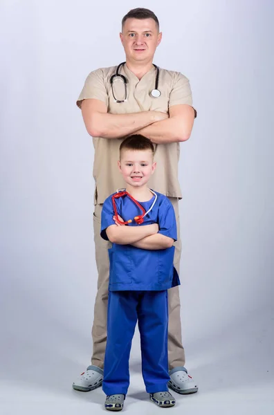 Father doctor with stethoscope and little son physician uniform. Medicine and health care. Future profession. Want to be doctor as dad. Cute kid play doctor game. Family doctor. Pediatrician concept