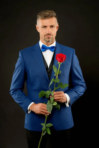 Ρομαντικός κύριος. Άνδρας ώριμη αυτοπεποίθηση macho με ρομαντικό δώρο. Όμορφος τύπος τριαντάφυλλο ρομαντικό ραντεβού λουλούδι. Καλοφτιαγμένο αντρικό κοστούμι. Κάνε καλή πρώτη εντύπωση. Ημέρα του Αγίου Βαλεντίνου και επέτειος — Φωτογραφία Αρχείου