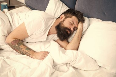 Biraz dinlenmeye ihtiyacım var. Uyku bozuklukları kavramı. Adam sakallı hipster uyku ile ilgili sorunlar yaşıyor. Yatakta yatan adam rahatlamaya ve uykuya dalmaya çalışır. Gevşeme teknikleri. Uyku ve uyanıklık ihlalleri