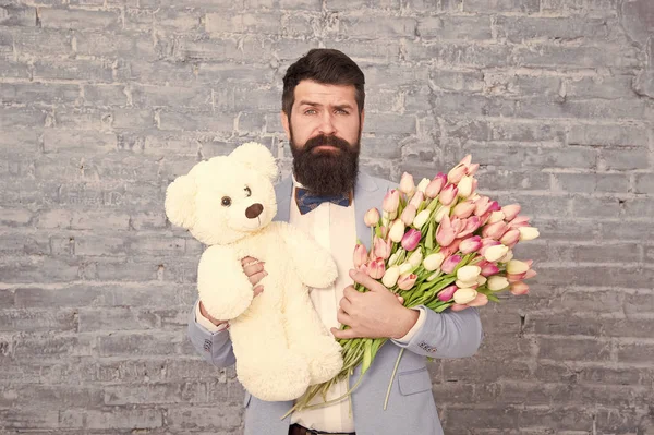 Surprise will melt her heart. Romantic man with flowers and teddy bear. Romantic gift. Macho getting ready romantic date. Man wear blue tuxedo bow tie hold flowers bouquet. International womens day — Stock Photo, Image