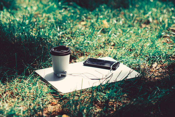 university students life. Online shopping. agile business. Online study. notebook with headset of mobile phone and coffee to go on green grass. working place outdoor. Free music. summer vibes. Relax