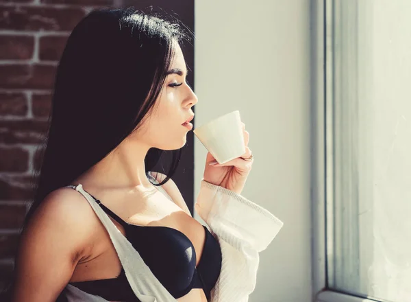 Mädchen sexy Brüste Kaffee trinken in der Nähe Fensterbank. attraktive weibliche Dessous, die sich zu Hause entspannen. perfekte Kaffeezeit. Aber erst einmal Kaffee. Ruhe und Frieden. Schluck cremigen Cappuccino. Morgenritual — Stockfoto