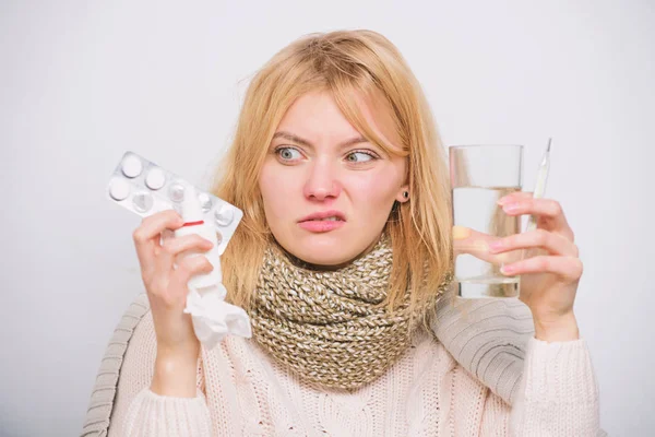 Hate to be ill. Ill woman treating symptoms caused by cold or flu. Cute sick girl taking anti cold pills. Unhealthy woman holding pills and water glass. Medication and increased fluid intake