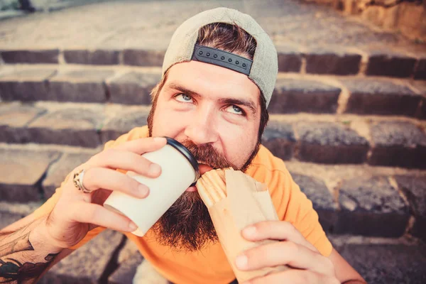 Homem barbudo comer salsicha saborosa. Nutrição de estilo de vida urbano. Comida de plástico. hipster despreocupado comer junk food while sit stairs. Um tipo a comer cachorros quentes. Lanche de bom humor. Apetite desencadeado. Conceito de comida de rua — Fotografia de Stock