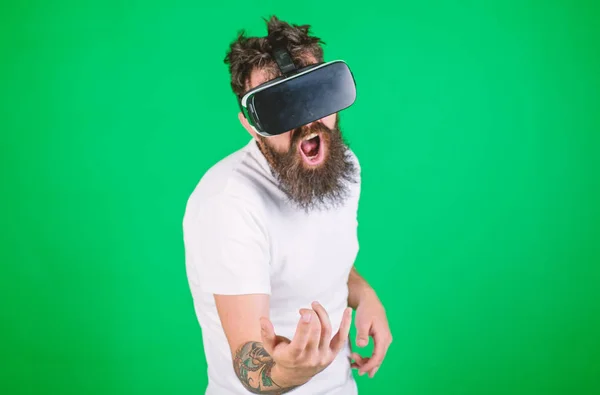 Guy with VR glasses learn to play music on guitar. VR musician concept. Hipster guitarist on enthusiastic face use modern technology for entertainment. Man with beard in VR glasses, green background