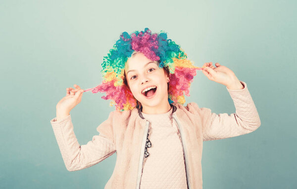 Playing with her hair. Funny kid with curly synthetic hair. Cute little girl with fancy hair. Adorable small child wearing bright clown hair wig