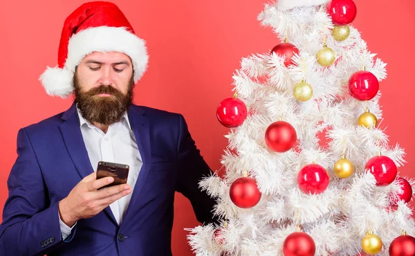 Homme barbu hipster porter costume formel et santa chapeau tenir smartphone. Envoyez un message de voeux de Noël mobile. Gestionnaire féliciter les collègues en ligne. Lisez les vœux de Noël. Bref vœux de Noël — Photo