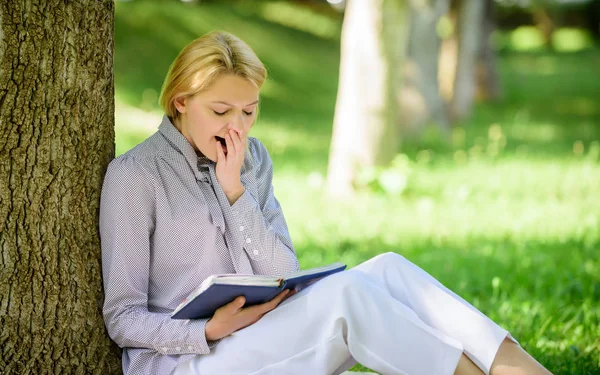 最好的女性自助书籍。女孩累打哈欠坐在公园瘦树干看书。阅读鼓舞人心的书籍。畅销书榜首。每个女孩都应该读的书。放松休闲是一种爱好概念 — 图库照片