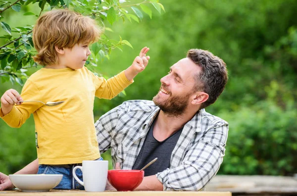 father and son eating outdoor. summer picnic. Morning breakfast. healthy food and dieting. Childrens day. happy fathers day. Little boy with dad eat cereal. family dinner time. Always happy together