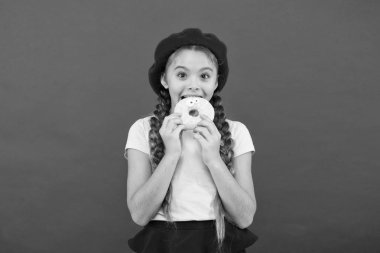 Çocuk gülümseyen kız donut yemeye hazır. Şeker dükkanı ve ekmek kavramı. Pişmiş Donuts büyük fanlar çocuklar. Resist taze yapılmış çörek için imkansız. Kız tutun sırlı tatlı çörek elinde kırmızı arka plan