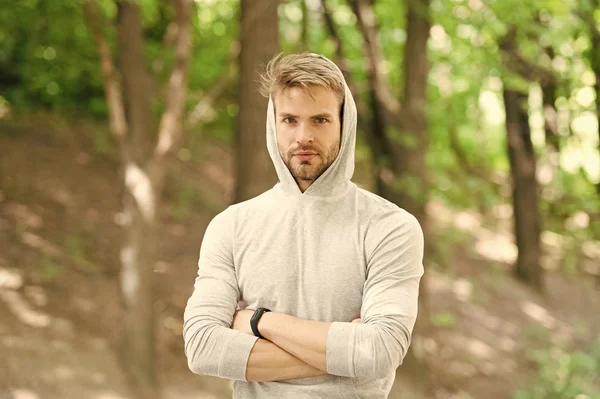 Feeling confident. Guy bearded attractive casual clothes hooded. Man with bristle confident face nature background defocused. Man unshaven guy looks handsome casual hooded. Comfortable means simple