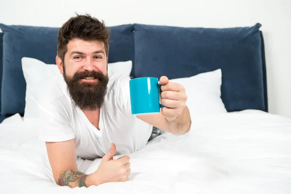 Full of energy. Coffee affects body. Man handsome hipster relaxing on bed with coffee cup. Bearded hipster enjoy morning coffee. Morning becomes much better with good coffee. Relax and rest