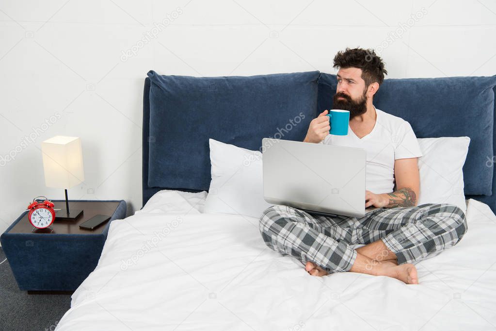 Hipster bearded guy pajamas freelance worker. Remote work concept. Social networks internet addiction. Online shopping. Man surfing internet or work online. Just woke up and already at work