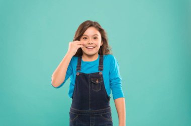 Genç teninin avantajları. Mutlu küçük kız mavi arka planda pürüzsüz bebek tenine dokunuyor. Sağlıklı taze yüz derisinde sevimli gülümsemesi olan küçük bir çocuk. Çocuk cilt bakımı kozmetik ürünleri