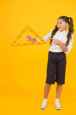 İki eşit kenarı olan üçgene bak. Mutlu küçük kız öğrenci sarı arka planda üçgen tutuyor. Geometri dersi için geometrik üçgen ile gülümseyen sevimli küçük çocuk. Üçgende ders olması