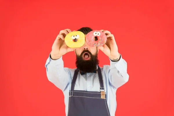 Sélection la plus savoureuse de beignets autour. Boulanger avec des beignets glacés. Homme barbu tenant beignets anneau sur fond rouge. Hipster avec beignets cuits dans les mains — Photo