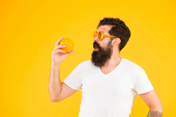 Healthy food taste better. Surprised hipster looking at healthy orange fruit on yellow background. Bearded man with healthy vitamin snack. Eat healthy, be nutrition wealthy