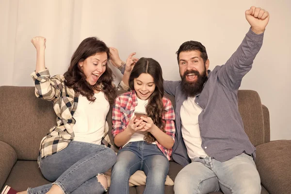Family spend weekend together. Child little girl use smartphone with parents. Friendly family having fun together. Mom dad and busy daughter relaxing on couch. Family leisure. Parental advisory