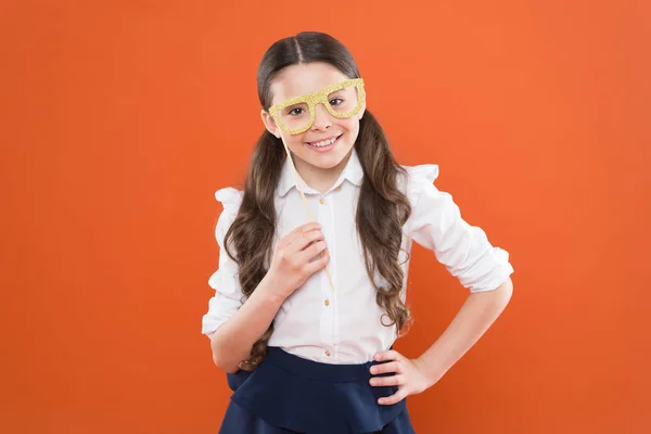 Was bedeutet es, intelligent zu sein? kleines intelligentes Schulmädchen auf orangefarbenem Hintergrund. Kleines Kind mit Brille im schicken Stil. Schulfest-Konzept. Kind schaut durch Fotoautomaten-Requisiten Brille — Stockfoto