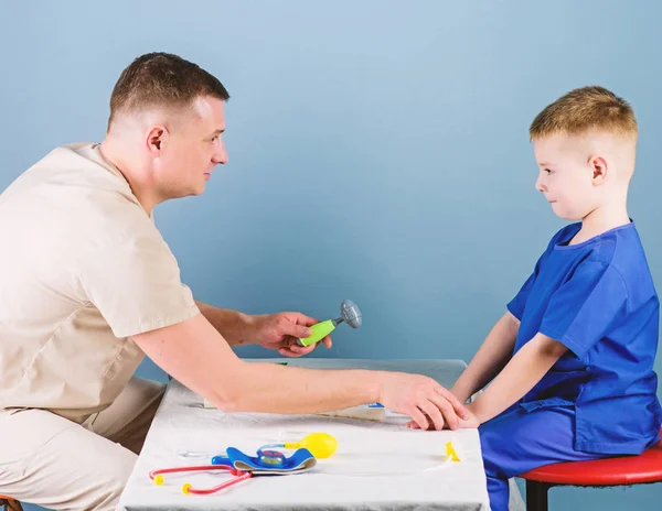 Salud. Cuidado de niños. El pediatra cuidadoso comprueba la salud del niño. Examen médico. Servicio médico. Hombre doctor sentarse mesa herramientas médicas examinando niño pequeño paciente. Concepto de pediatra —  Fotos de Stock