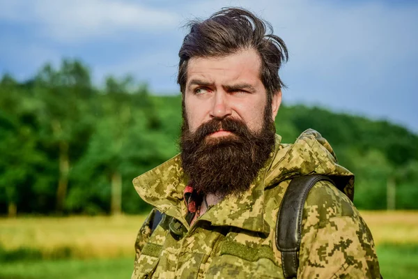 Um homem sério. soldado de uniforme militar. Um caçador furtivo brutal. Cuidado com a barba masculina. homem barbudo caminhando com mochila. hipster maduro com barba em jaqueta militar. Homem caçador. Temporada de caça — Fotografia de Stock