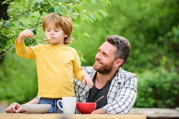 Food habits. Little boy with dad eating food picnic yard nature background. Summer breakfast. Healthy food concept. Family weekend. Father son eat food and have fun. Menu for children. Homemade meal — Stock Photo, Image