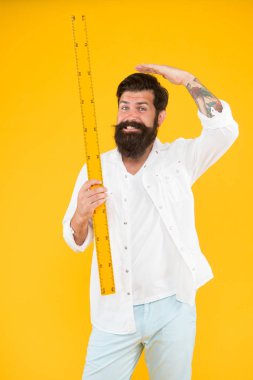 Cetvel ile yüksekliğini ölçüyor. Okul öğretmeni veya üniversite öğrencisi sarı arka plan üzerinde cetvel tutan. Sakallı adam metrik cetvel ile ölçüm alıyor. Benim cetvelim seninkinden daha uzun.