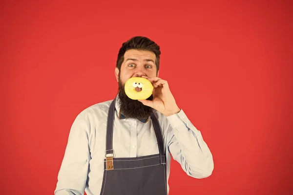 Hipster padeiro barbudo segurar donut vitrificado no fundo vermelho. Fatos verdadeiros sobre o açúcar. Nem pensar. Conceito de café e padaria. Doce donut do padeiro. homem barbudo padeiro em cozinhar avental segurar bonito sobremesa — Fotografia de Stock