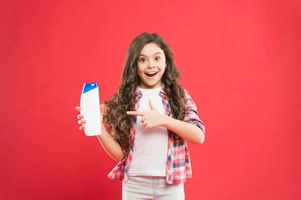 Die beste Seife für Kinderhaut. kleines Kind mit langen lockigen Haaren, das mit dem Finger auf Seife auf rotem Hintergrund zeigt. kleines Mädchen mit Flüssigseife in der Flasche zum Waschen in der Badewanne oder Dusche. Wellness-Seife — Stockfoto