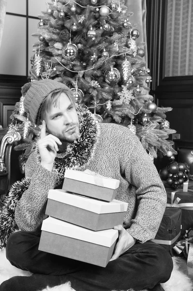 Macho con cara pensante en sombrero, suéter sujetar regalos envueltos — Foto de Stock