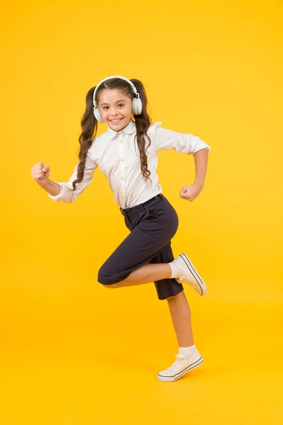 Ενεργητική επιστροφή στα σχολικά τραγούδια που θα σε κάνουν να μετακομίσεις. Το παιδί με την ενέργεια τρέχει στο σχολείο με κίτρινο φόντο. Μικρό κορίτσι που απολαμβάνει την ενεργητική μουσική στα ακουστικά. Ενεργός και ενεργητικός — Φωτογραφία Αρχείου