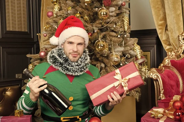 Hope this season finds you all wrapped up in happy. Happy man with new year gift box. Guy is celebrating new year at home. Merry Christmas and Happy New Year. Man in santa hat hold new year present