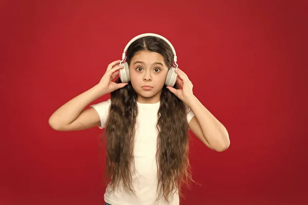 What is all this about. Small girl wearing stereo headphones. Cute music fan with wireless headset. Little child using technology for leisure or education. Little girl listening to music