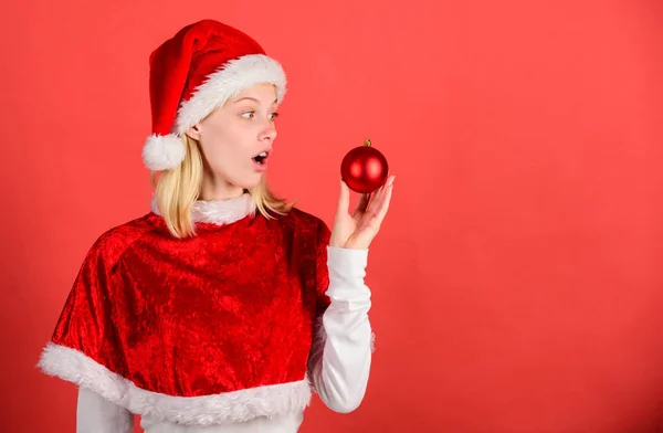 圣诞乐趣。女孩快乐穿圣诞老人服装庆祝圣诞节举行球装饰红色背景。享受庆祝新年快乐。圣诞节准备概念。最喜欢的时间年圣诞节 — 图库照片