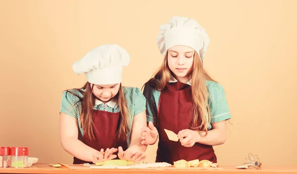 Grembiuli per bambini e cuoco cappelli da cucina. Biscotti fatti in casa meglio. Ricetta di famiglia. Abilità culinarie di cucina. Cucinare biscotti allo zenzero. Ragazze sorelle divertirsi pasta allo zenzero. Bambini che cucinano biscotti insieme — Foto Stock