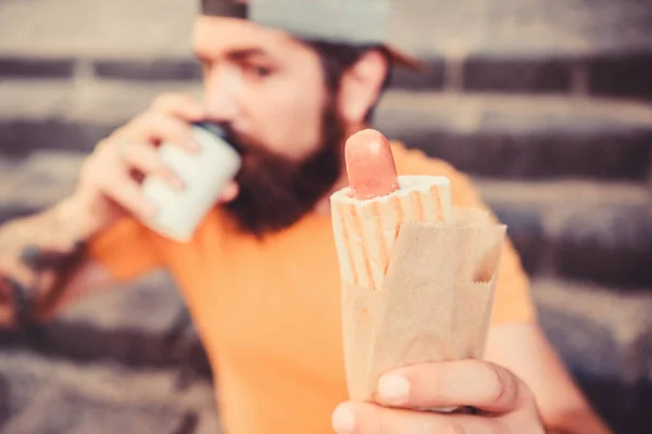 Street food so good. Urban lifestyle nutrition. Carefree hipster eat junk food while sit on stairs. Hungry man snack. Junk food. Guy eating hot dog. Man bearded bite tasty sausage and drink paper cup