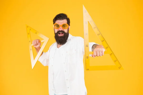 Haciendo divertida la geometría. Funny hipster usando herramientas geométricas en geometría. Profesor de geometría sosteniendo triángulos para la lección escolar sobre fondo amarillo. Geometría de aprendizaje o enseñanza del hombre barbudo — Foto de Stock