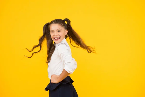 Выглядишь счастливым. Счастливая маленькая девочка улыбается в школьной форме на оранжевом фоне. Веселый маленький ребенок со счастливой улыбкой и модным взглядом. Очаровательный ребенок наслаждается счастливой школьной жизнью, копирует пространство — стоковое фото