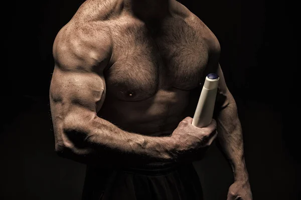 Mano bodybuilder muscolare tiene bottiglia di plastica. Prodotto per la cura della pelle. Sportivo toracico muscoloso su bakground nero. Prodotto per la cura del corpo e il trattamento della pelle. Lozione per il corpo maschile. Lozione igienica cosmetica — Foto Stock