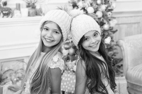 Moderní dívky. Zimní sezóna příslušenství. Děti nosí pletené čepice. Šťastný úsměv dívky dlouhé vlasy stojí vánoční strom pozadí. Děti nosí teplé měkké pletené růžové klobouky. Efektní pletené čepice pro dívky — Stock fotografie