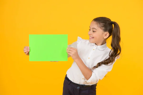 Glorieuse couleur. Petite fille tenant une feuille de papier vide sur fond jaune. Petit enfant avec un livre vert vierge pour l'affectation ou le travail de projet. Papier d'examen. Copier du papier, espace de copie — Photo